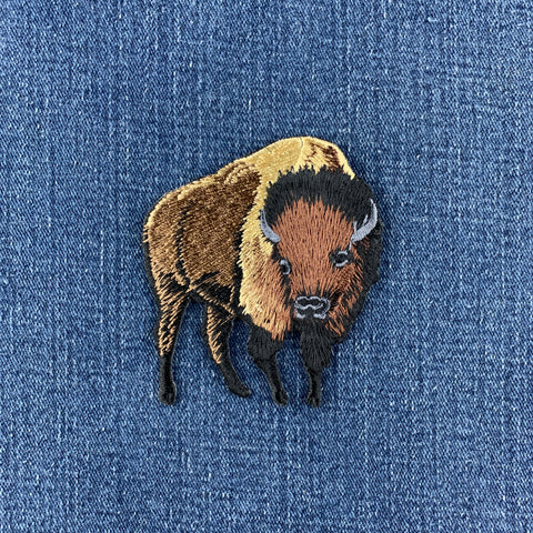 Embroidered buffalo applique patch with a brown, black, and beige design on a denim background.