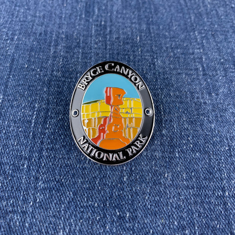 An oval enamel Walking Stick Medallion featuring a Bryce Canyon National Park design, displayed on a blue denim fabric background.