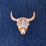 A embroidered bull skull patch with a southwestern longhorn design displayed on a denim background