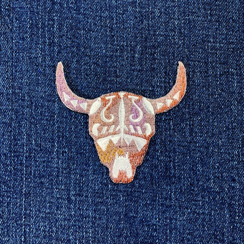 A embroidered bull skull patch with a southwestern longhorn design displayed on a denim background