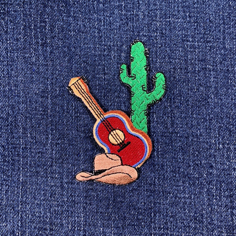 Embroidered patch of a guitar and cactus on denim fabric