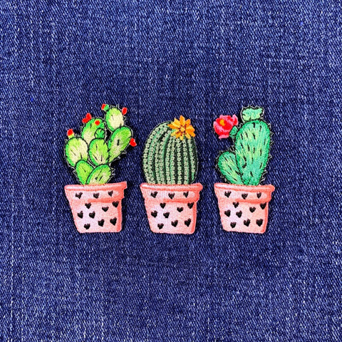 Three embroidered cactus plants in pots on a denim background