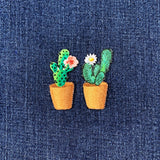 Two embroidered cactus plant patches with flowers on a denim background