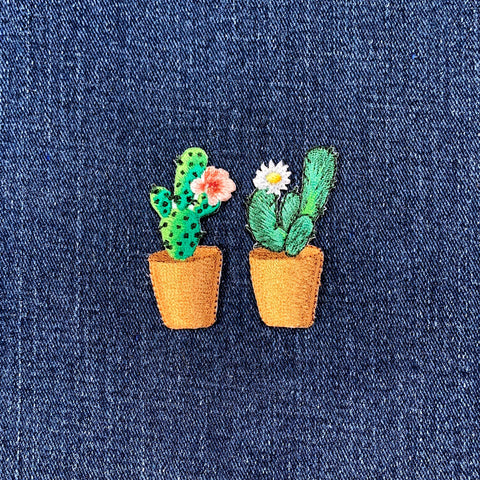 Two embroidered cactus plant patches with flowers on a denim background