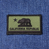 Subdued tactical patch of the California Republic flag, showing a dark bear and star on an olive green background, on blue denim.
