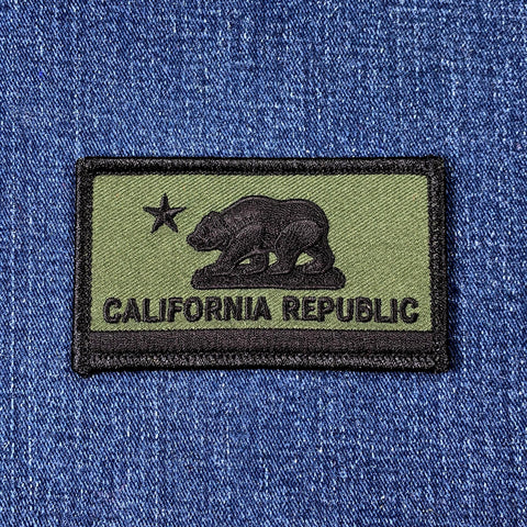 Subdued tactical patch of the California Republic flag, showing a dark bear and star on an olive green background, on blue denim.