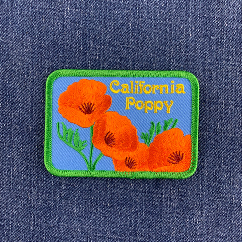 A rectangular patch featuring orange California poppies with green leaves on a blue background, and the text 'California Poppy' is embroidered at the top and displayed on a denim background