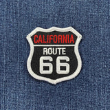 A shield-shaped patch with 'California Route 66' text embroidered in black, white, and red colors on a denim background