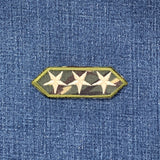 A patch featuring three white stars on a camouflage fabric, displayed on a denim background.