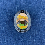 An oval enamel Walking Stick Medallion featuring a landscape illustration of Capitol Reef National Park, displayed on a blue denim fabric background.