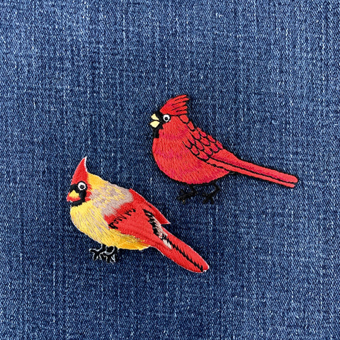 Two embroidered red cardinal patches on a denim background