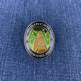 A circular enamel Walking Stick Medallion of Carlsbad Caverns National Park, featuring a gold-toned stalactite and green cave background, set against a blue denim fabric background.