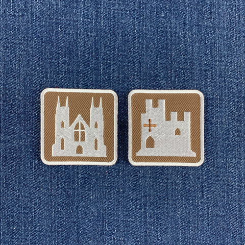 two embroidered patches on a denim background: a castle patch and a cathedral patch resembling European road signs