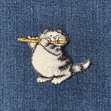 Embroidered patch of a cat holding a flute on denim fabric