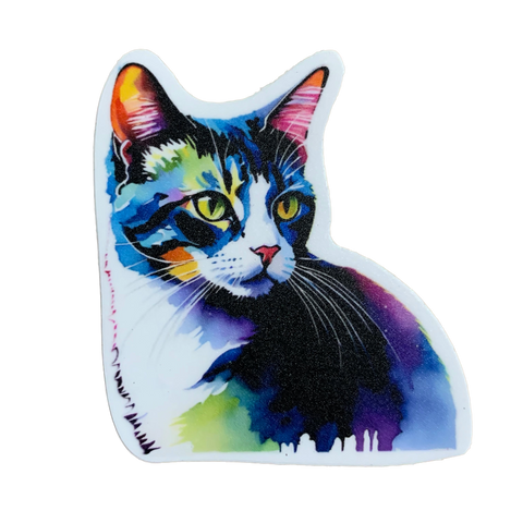 A die-cut sticker in the shape of a cat's head and chest, featuring an abstract watercolor portrait of a tabby cat. The cat's fur is depicted in vibrant, saturated colors including blue, purple, pink, and yellow. The sticker is placed on a wooden surface.