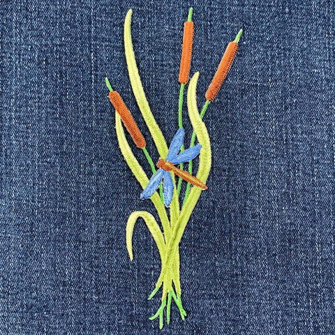 Embroidered design of a dragonfly and cattails on denim fabric