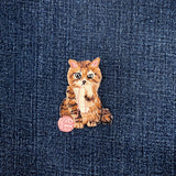 cat with pink yarn patch on a blue denim background