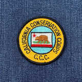 A round vintage patch featuring the California Conservation Corps emblem on a denim background