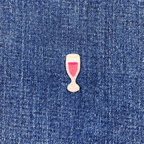 Embroidered patch of a glass with sparkling wine on blue denim fabric