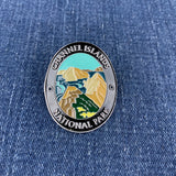 An oval enamel Walking Stick Medallion featuring a landscape design of Channel Islands National Park, placed on a blue denim background.