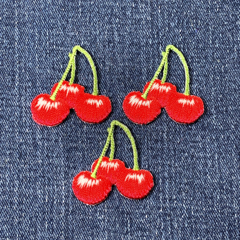 Three red cherry patches on a denim background