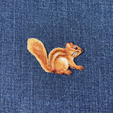 An embroidered brown and orange chipmunk patch on a blue denim fabric background.