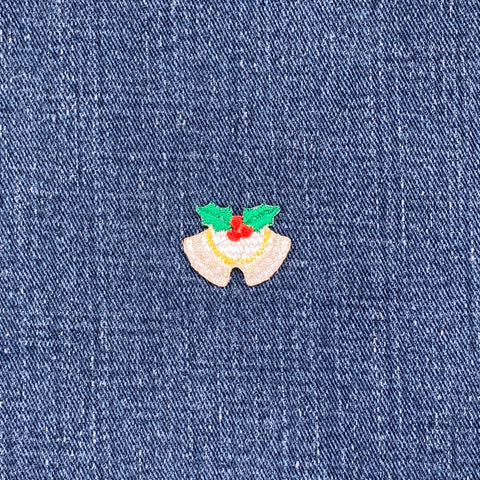 Embroidered patch of Christmas bells with holly leaves and berries on blue denim fabric.