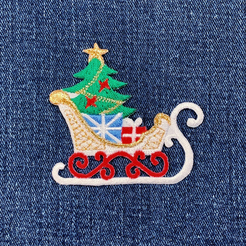 Embroidered Christmas patch on denim fabric with a sleigh, tree, and presents.