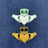 a green and white Claddagh and a black and gold claddagh patch on blue denim fabric