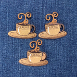 Three embroidered coffee cup and saucer patches on a denim fabric background.