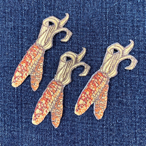 Three embroidered corn patches on a denim background
