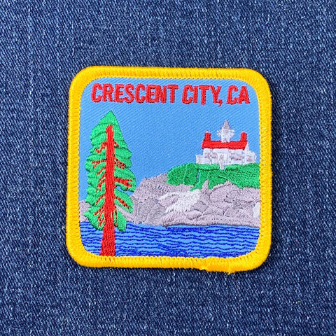 A patch featuring an illustration of a lighthouse, tree, and surrounding landscape with the text 'CRESCENT CITY, CA'.
