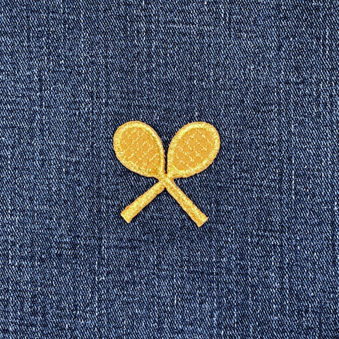 Two gold tennis rackets patches on a blue denim fabric.