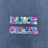 A sequin cheerleading badge and a sequin dance badge spelling out the word 'CHEER' and 'DANCE' with multicolored sequins on a denim background.