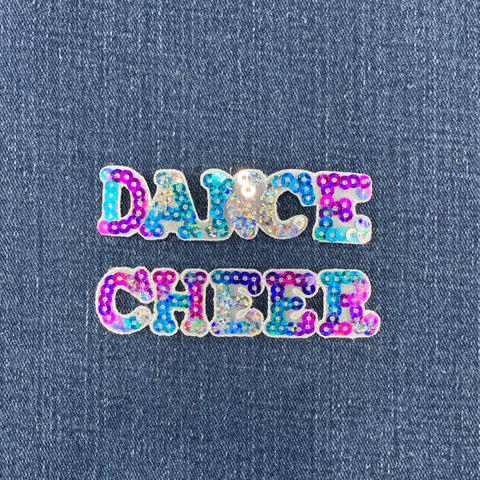 A sequin cheerleading badge and a sequin dance badge spelling out the word 'CHEER' and 'DANCE' with multicolored sequins on a denim background.