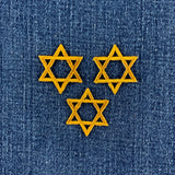 Three yellow embroidered Star of David patches arranged in a triangle on a blue denim fabric background.