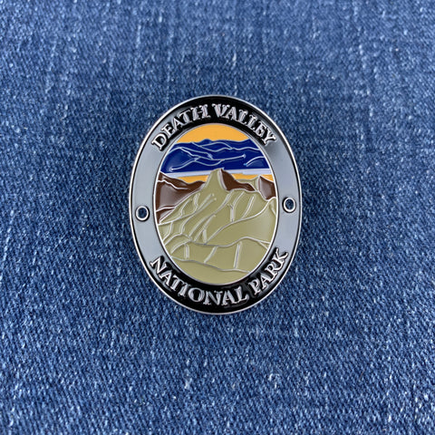 An oval enamel medallion featuring Death Valley National Park, resting on a blue denim fabric background.
