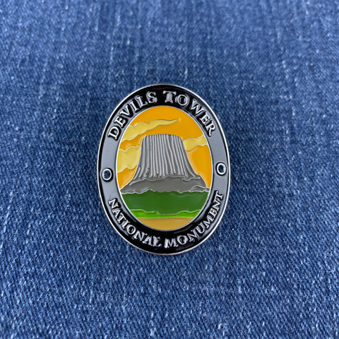 An oval enamel Walking Stick Medallion featuring a scenic illustration of Devil's Tower National Monument, displayed on a blue denim fabric background.