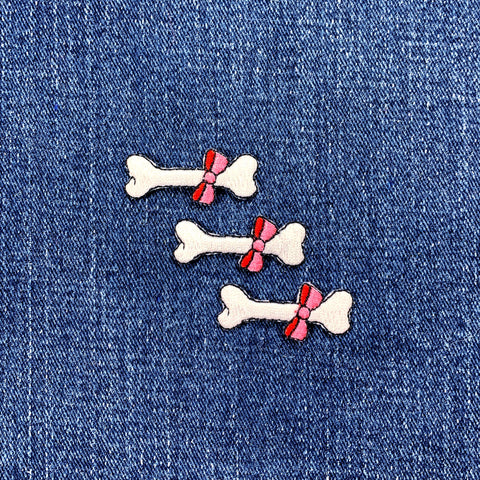 Three bone-shaped patches with pink bows on a denim background