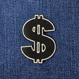 Black dollar sign patch on blue denim fabric