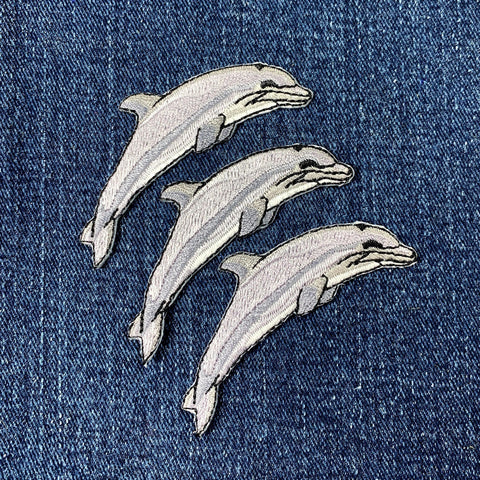 Three dolphin patches on a denim fabric background