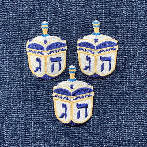 Three embroidered dreidels on a denim background