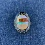 An oval enamel Walking Stick Medallion featuring the Dry Tortugas National Park emblem, displayed on a blue denim fabric background.