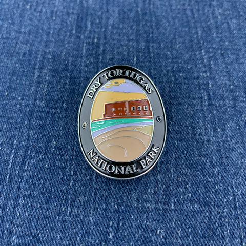 An oval enamel Walking Stick Medallion featuring the Dry Tortugas National Park emblem, displayed on a blue denim fabric background.