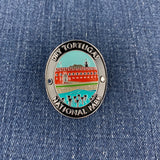 An oval enamel Walking Stick Medallion featuring a colorful illustration of Dry Tortugas National Park, including a red building, lighthouse, and turquoise water, with the text 'DRY TORTUGAS NATIONAL PARK' on a blue denim background.