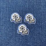 Three small, identical embroidered patches depicting a silver film reel with a strip of black and white film in the foreground, outlined in blue on a denim background