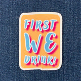 Sticker with 'FIRST WE DRINK!' text on a denim background