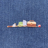 A small patch shaped like a tackle box and fishing pole shown on a blue denim fabric background.