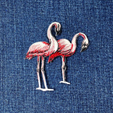 A pair of pink flamingos applique patches with a shimmery texture on a denim background