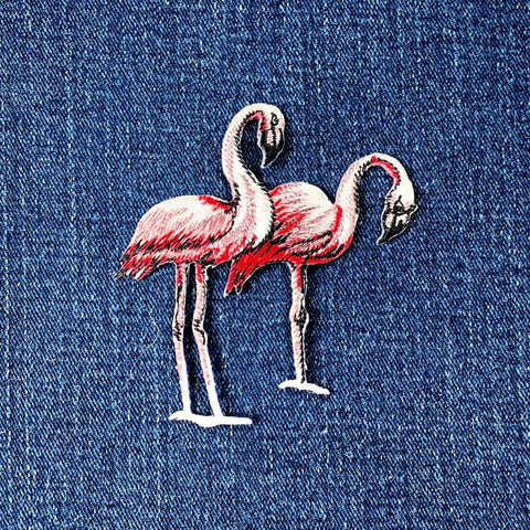 A pair of pink flamingos applique patches with a shimmery texture on a denim background